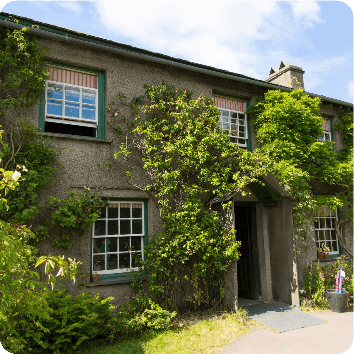 Georgian-style house covered in greenery, located in the scenic Lake District, ideal for tours from London.