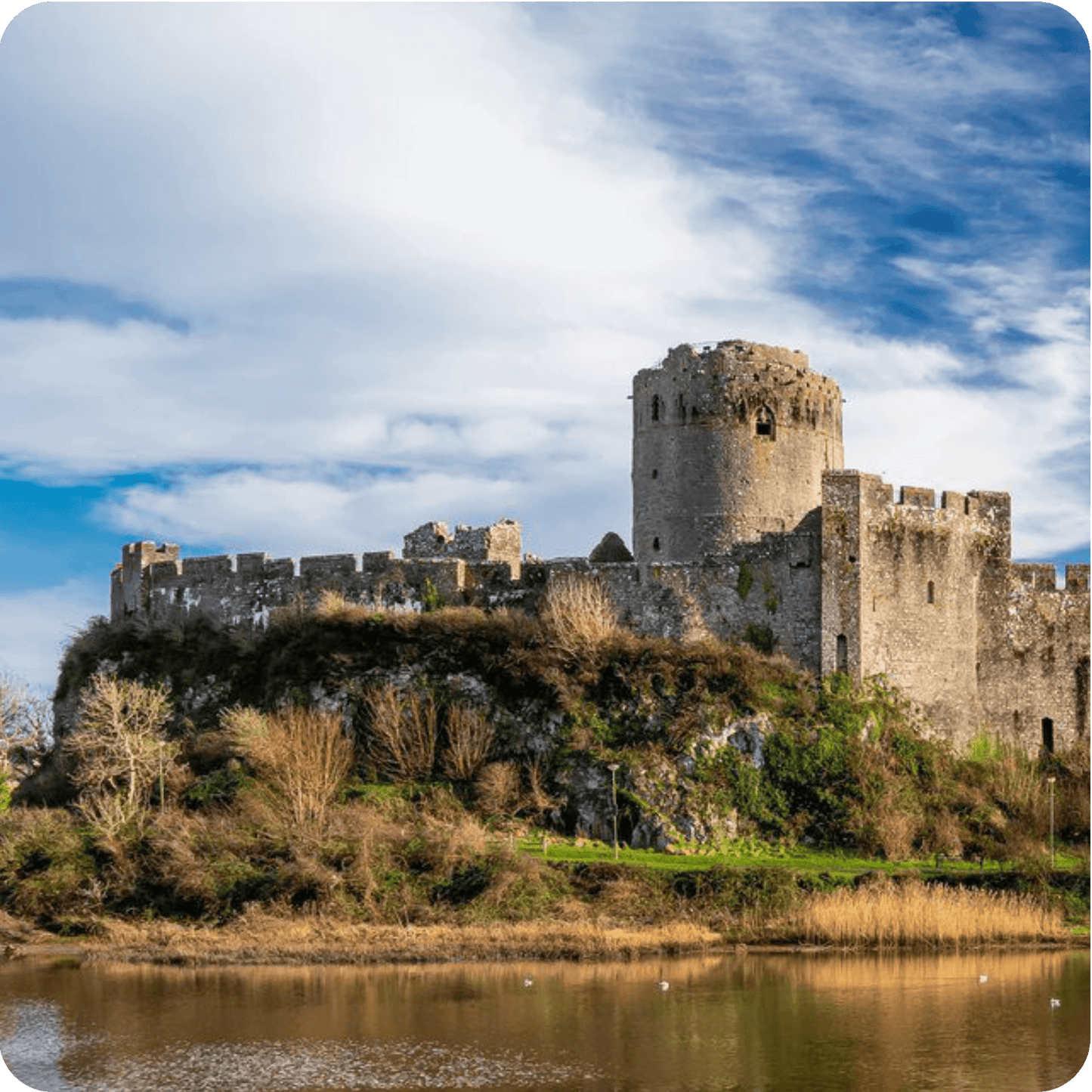 Mysterious castle ruins beside calm waters in Wales, showcasing historic architecture and natural beauty.